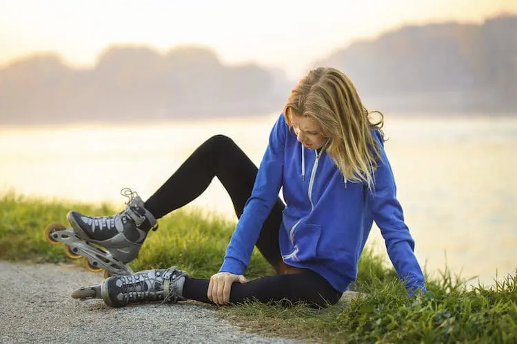 Woman on the ground holding her ankle, wearing roller skates.