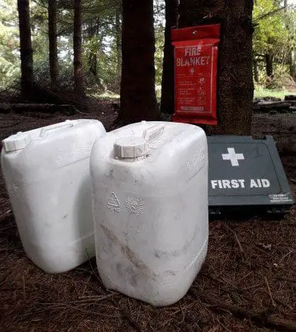 Some water bottles, a fire blanket and first aid kit in a woodland setting.