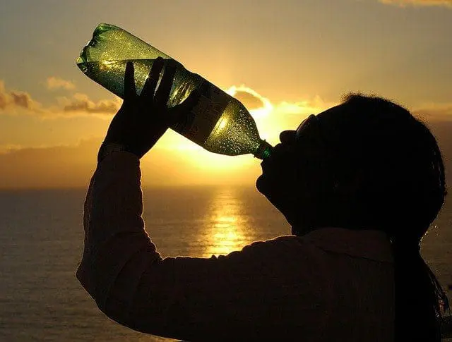 A person drinking from a large water bottle with a sunset in the background.