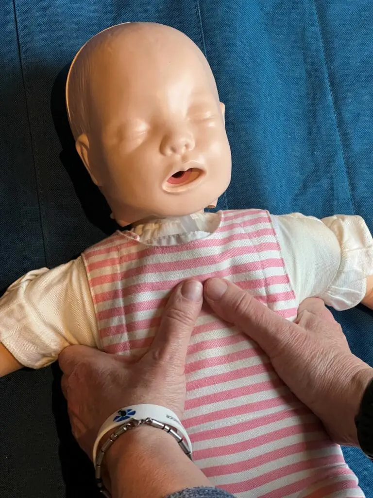 CPR demonstration on an infant manikin showing two thumbs in centre of the chest