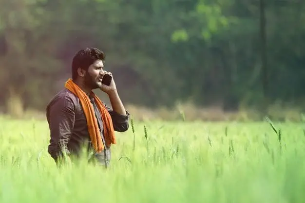 Man wearing orange scarf in a field of tall grass on a mobile phone