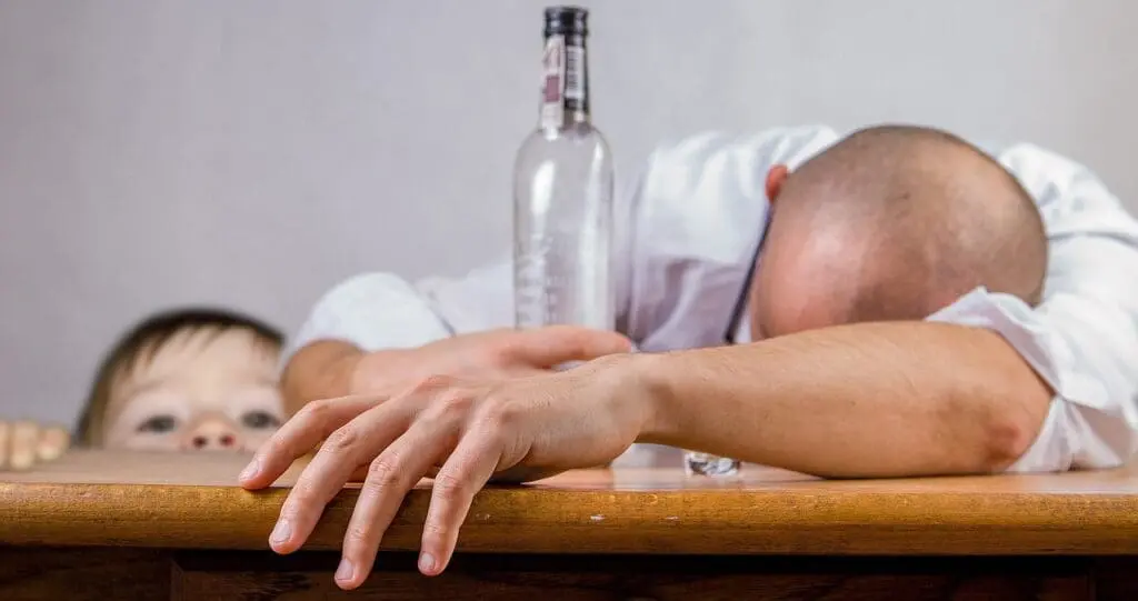A man slumped with an empty bottle and a child looking on