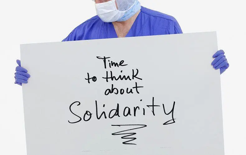 A doctor in scrubs holding up a solidarity sign