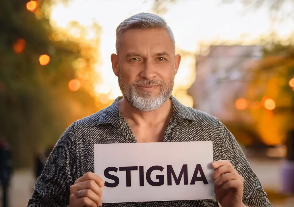 A man holding up a sign that says 'stigma'. Mental health image.
