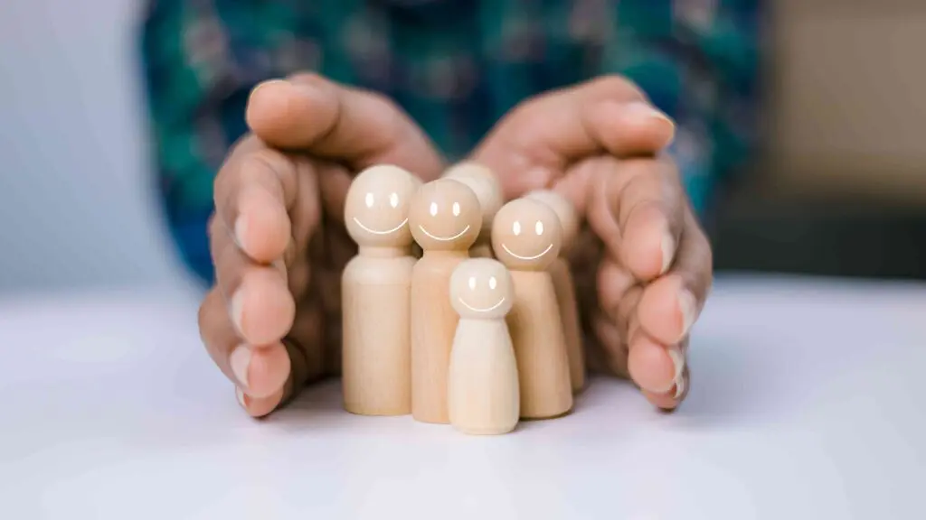 Two hands guarding little wooden people