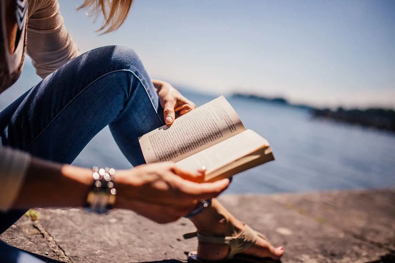A woman sitting by the sea reading a book - mental health