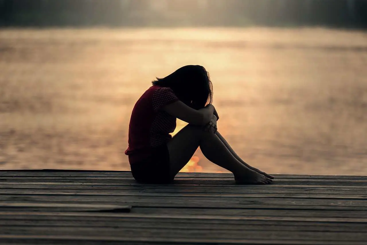 A girl sitting alone outdoors with head in hands. Sunset.
