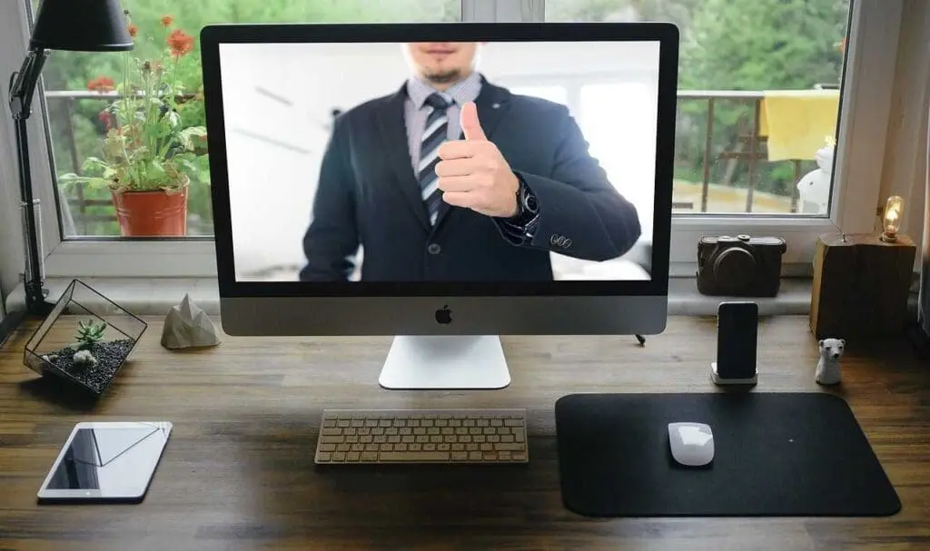 A home office set up with a man on the screen giving a thumbs up.