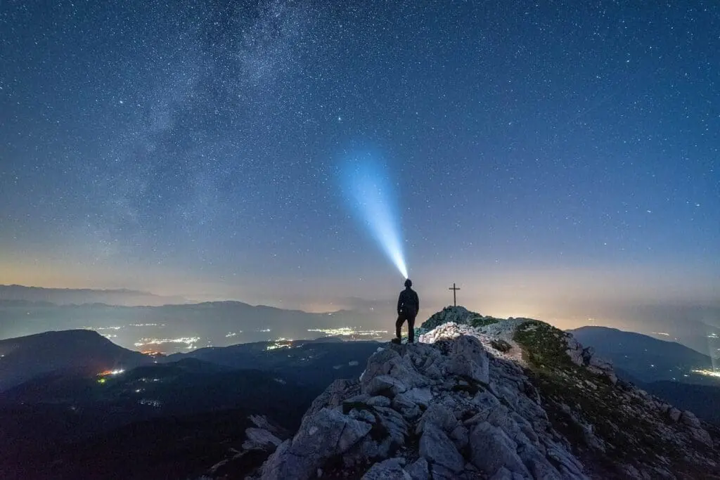 A person on a hilltop with a bright torch shining into the distance