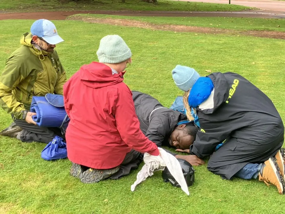 Three people learning first aid kneeling next to a colleague playing the injured party.