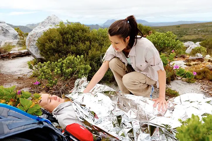 Injured woman under foil blanket while friend watches over her