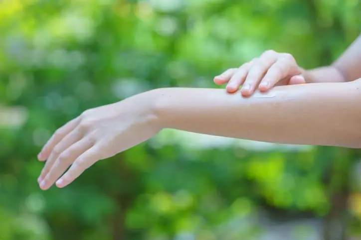 Woman applying sun lotion to her arm with a garden backdrop. First aid for gardeners.