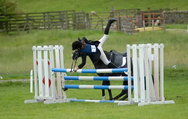 Horse rider falling over head of horse at jump